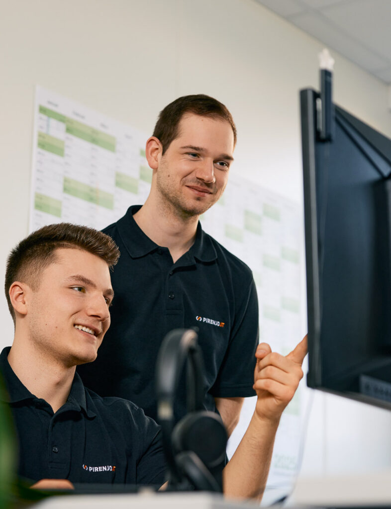 Zwei IT-Mitarbeiter im Gespräch vor einem Bildschirm.