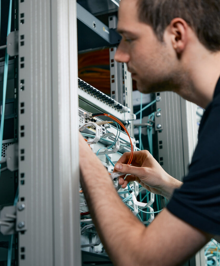Techniker arbeitet an Netzwerkkabeln im Serverschrank.